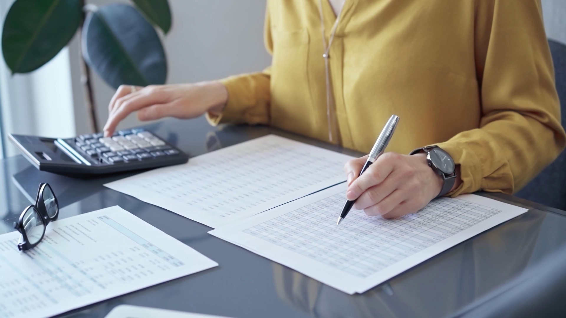 Professional business woman in yellow blouse is working on financial reports. Close-up of a woman's hands using calculator for audit or accounting